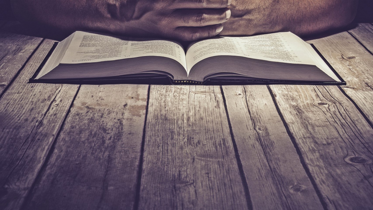 Man praying on a wooden table with an open Bible.